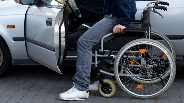 Homem com deficiência saindo da cadeira de rodas para entrar no carro