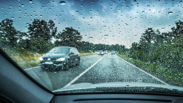 Condutor dirigindo carro com pneu desgastado em dia chuvoso