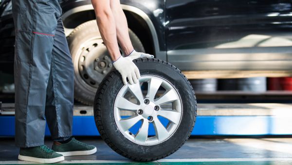 Mecânico levando pneu de carro para outro local da oficina