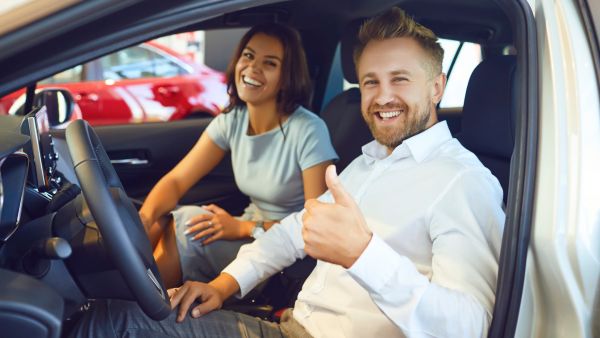 Casal feliz após adquirir carro usado em revendedora