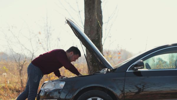 Homem avaliando se há problemas no carro na estrada