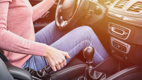 Mulher soltando o freio de mão do carro para voltar para a estrada