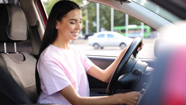 Mulher sorrindo prestes a ligar o carro e liberar o freio de mão para ir ao seu destino