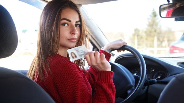 Nova condutora dentro do carro com uma mão no volante e outra segurando cnh