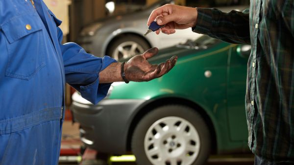 Condutor entregando chave do carro ao mecânico de oficina mecânica de confiança para consertar câmbio