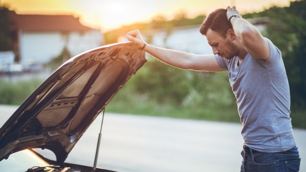 Homem olhando componentes internos do carro após problema de funcionamento