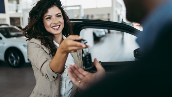 Mulher feliz entregando chave para comprador após fechar negócio sem deixar desvalorizar seu carro