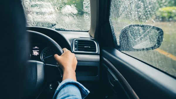 Pessoa dirigindo na chuva mantendo distância segura do carro da frente