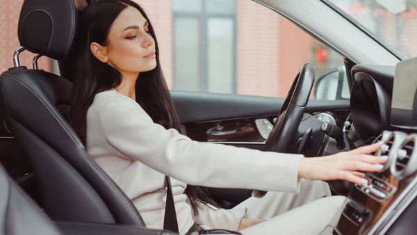 Mulher acionando ar condicionado automotivo enquanto dirige